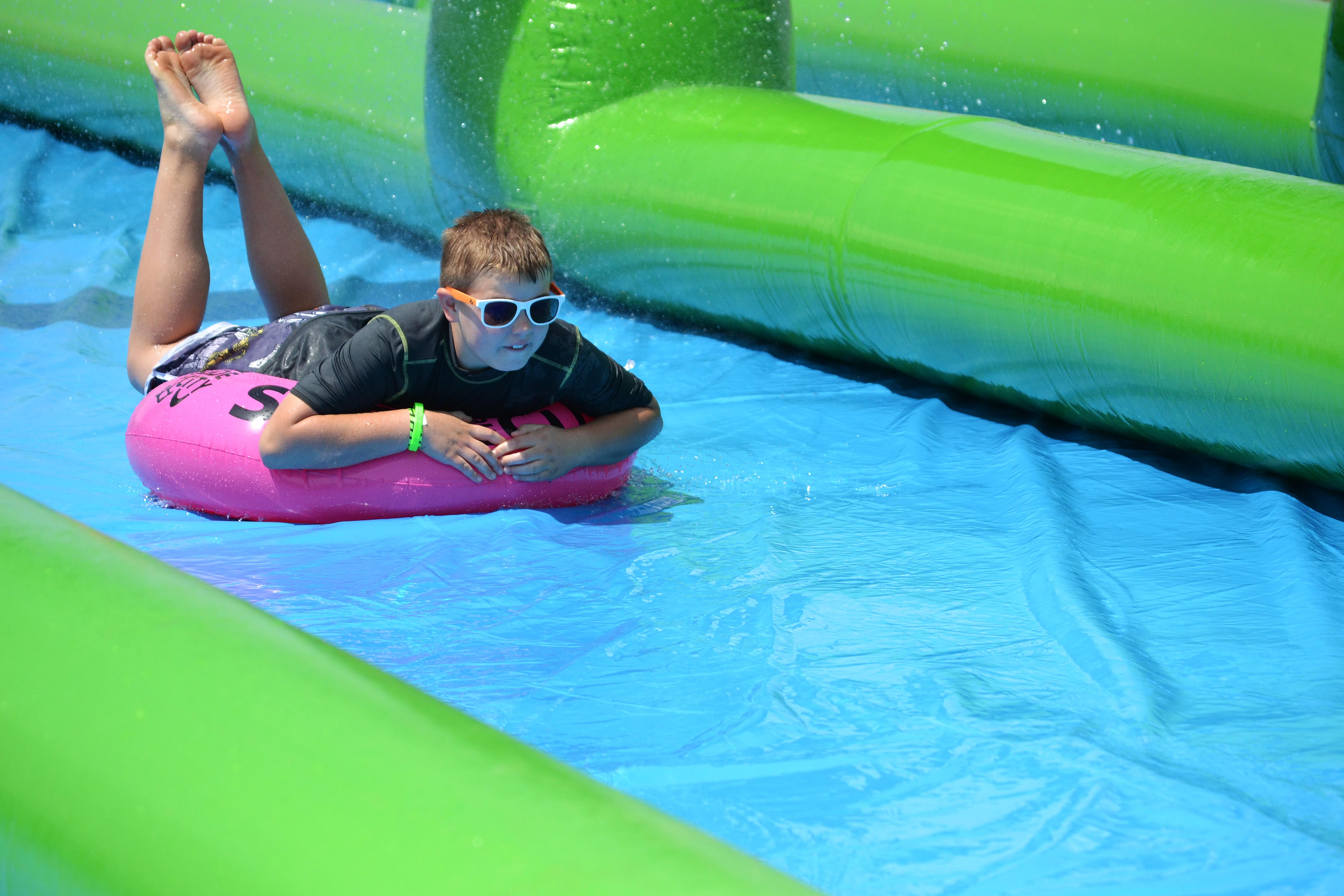 A young boy on an innertube skims across a colorful slip and slide