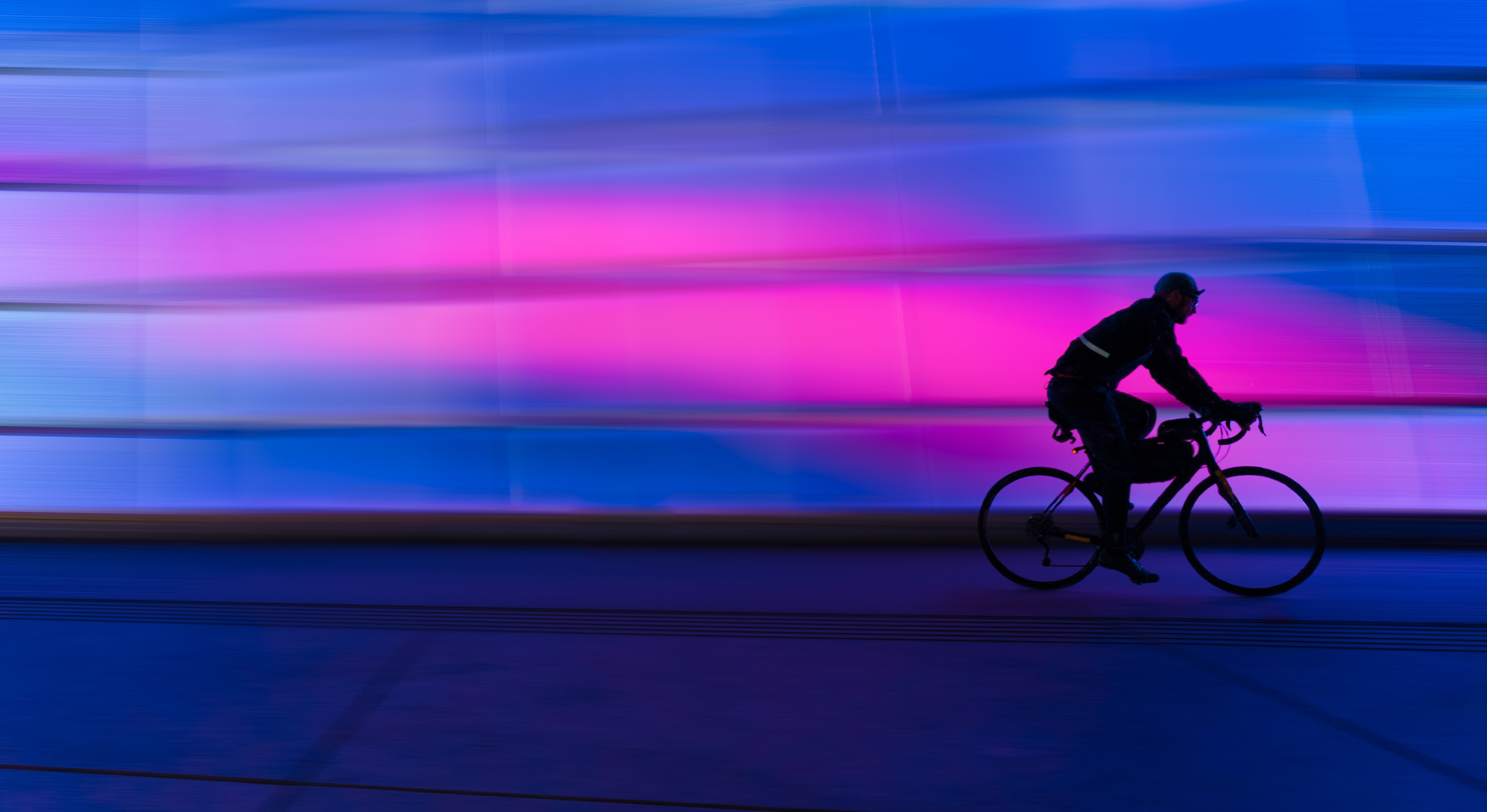 silhouette of a person riding a bike with a neon blue and pink background