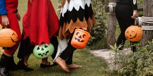 Four children dressed in halloween costumes carry plastic jack-o-lantern buckets as they walk on the grass