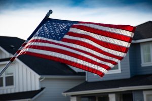 An American flag blowing in the wind with a row of homes in the background