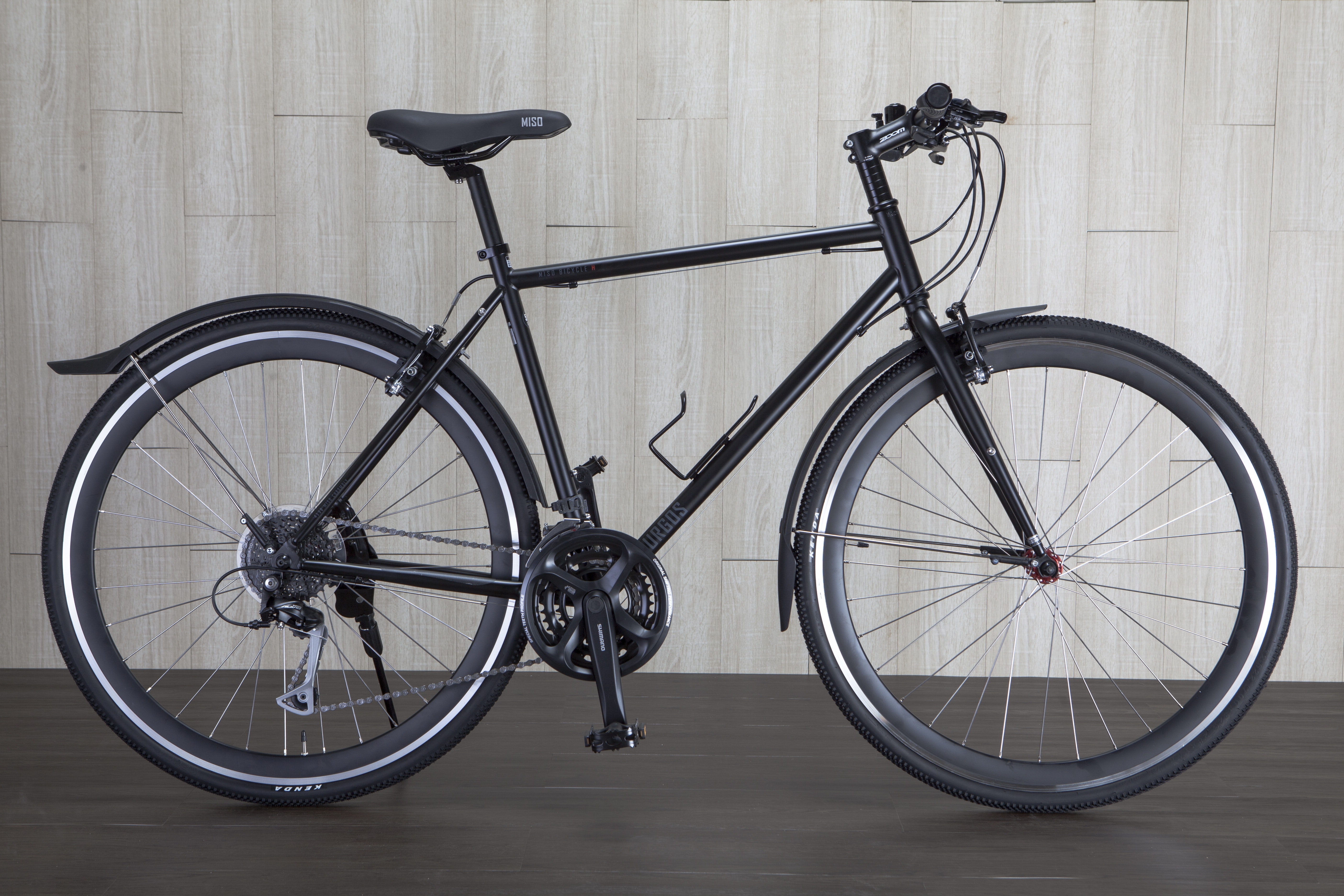 A bicycle with a black bike frame sits in front of a wall with light gray wooden panels and dark wood floors