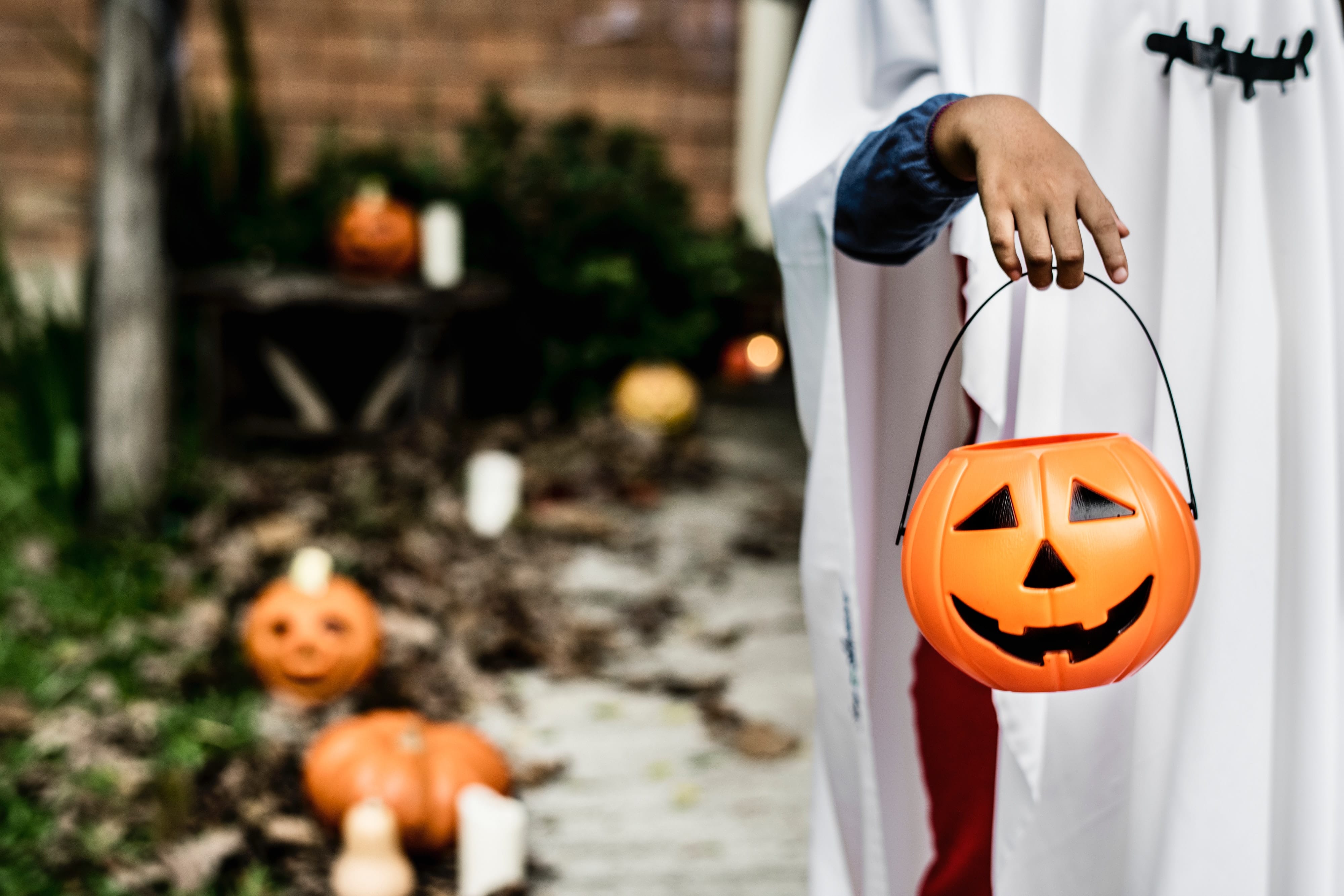 Child dressed in costume holds out a pumpkin pail during a stop on the trick-or-treat trail