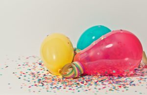 Yellow, pink, and blue party balloons lay on top of multi-colored confetti
