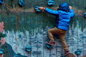 A boy climbs a rock wall with a mountain scene painted in the background.