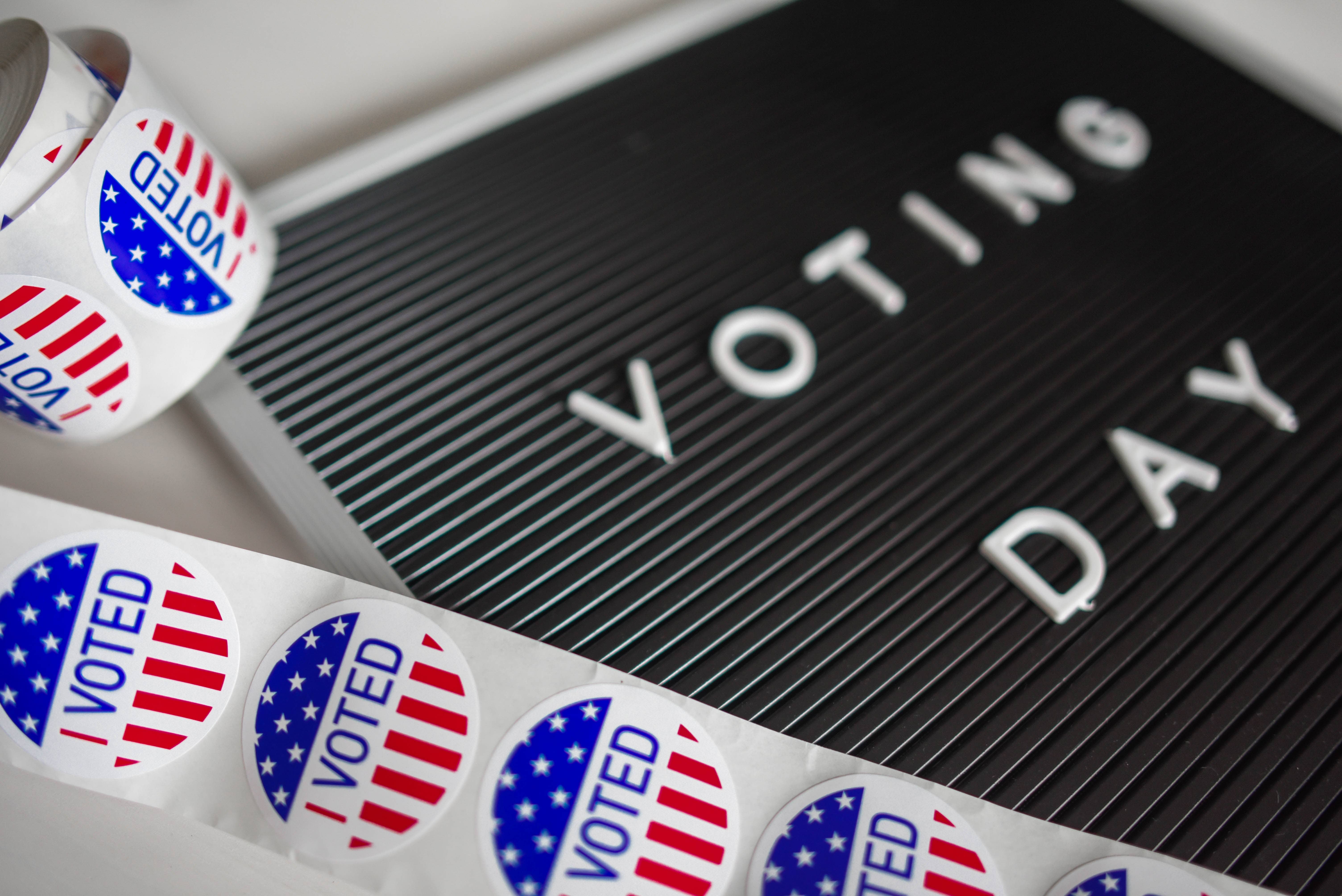 A roll of patriotic stickers with the words "I Voted" sits on top of a black board with the words "Voting Day" written across it.