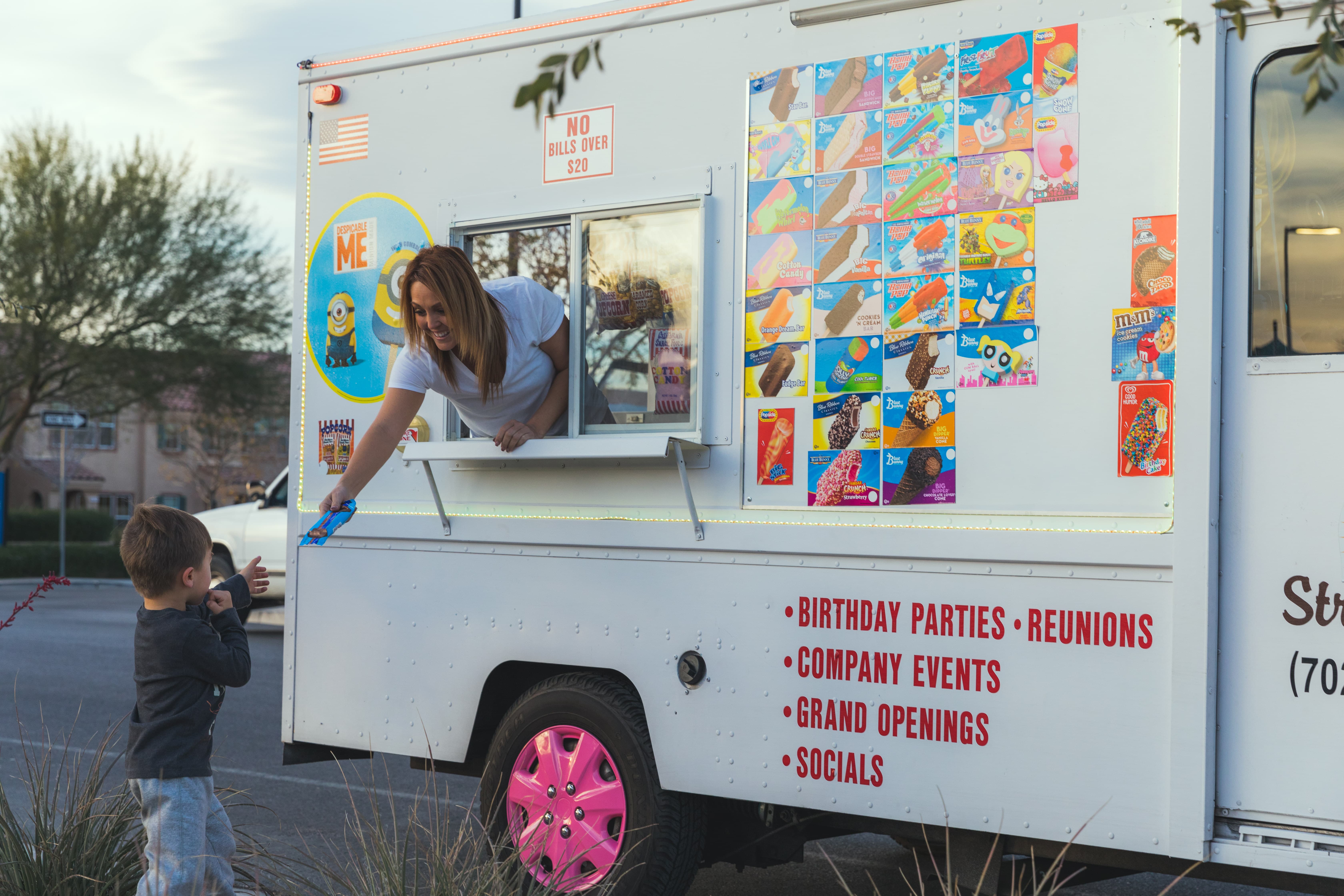 A woman hands a child a popsicle from the Street Freeze ice cream truck