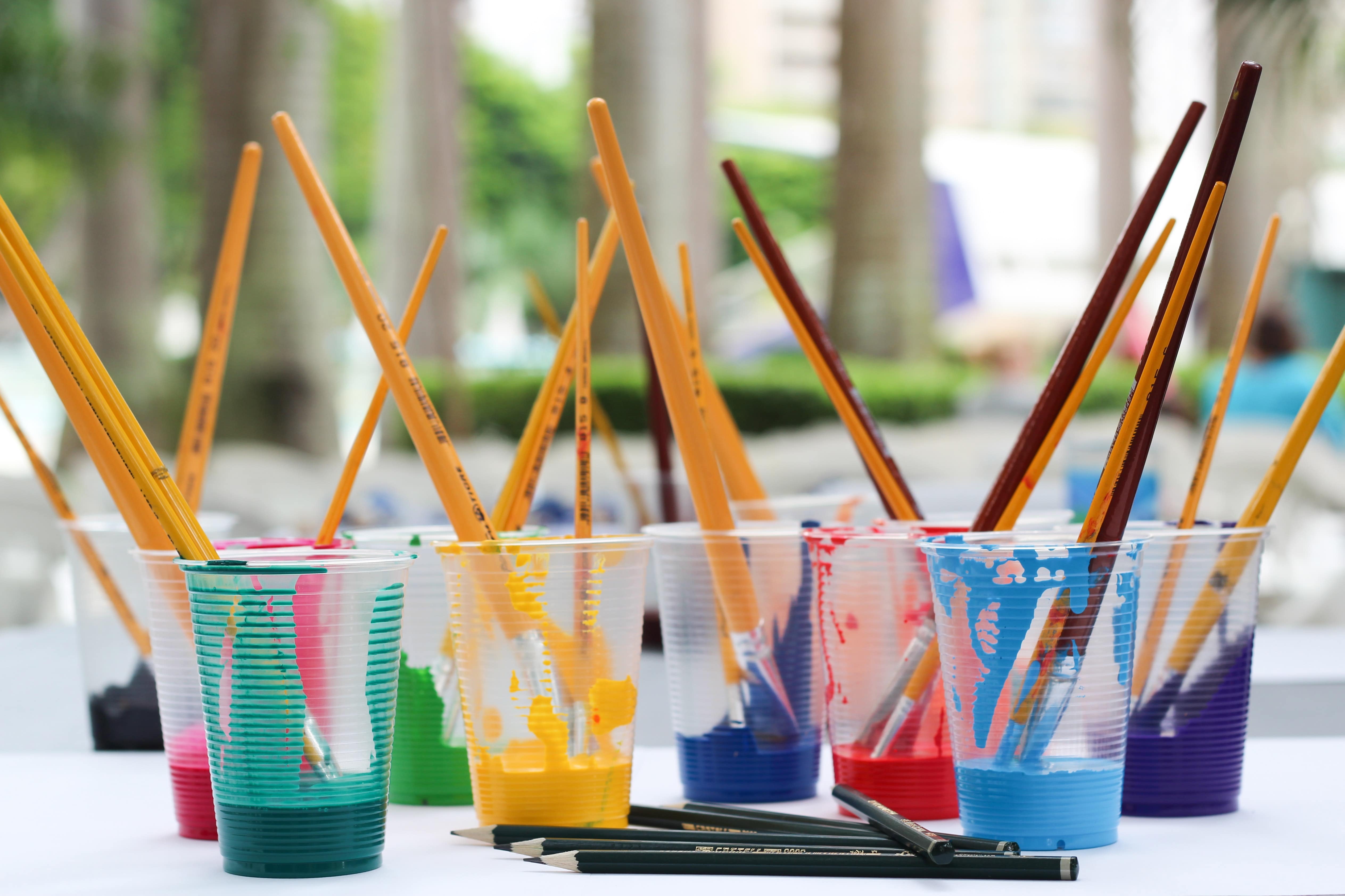 Cups of different colors of paint and brushes sit on a table