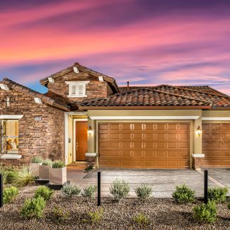 Exterior of stone house with landscaping and sunset sky.