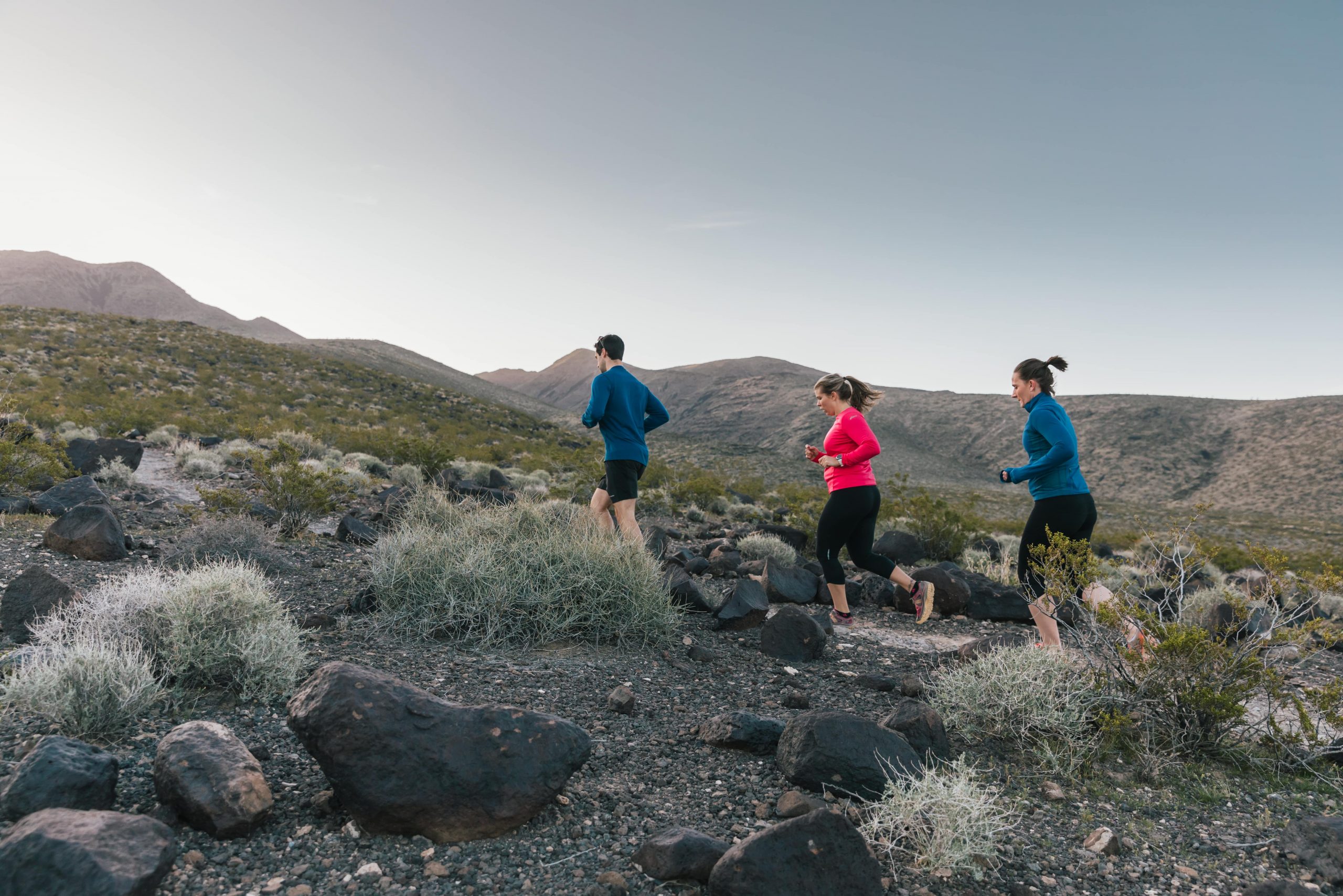 Two women and a man run on a trail